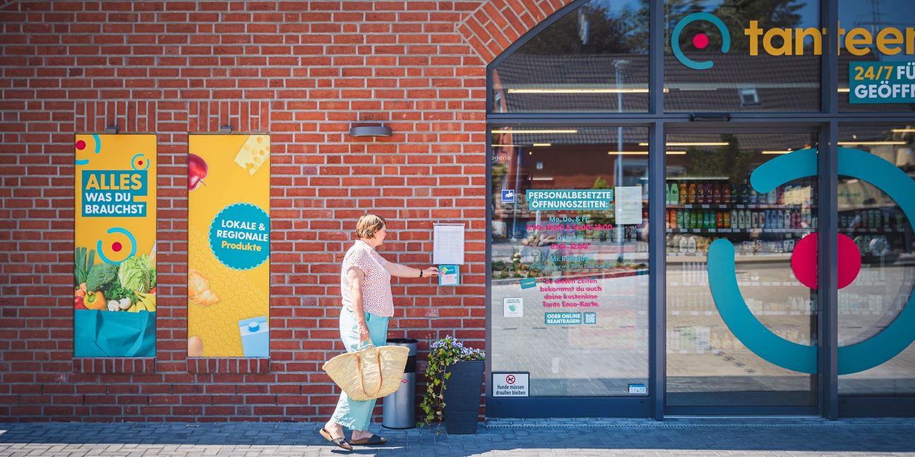 Frau mit Einkaufstasche öffnet Supermarkttür mit Zugangskarte.