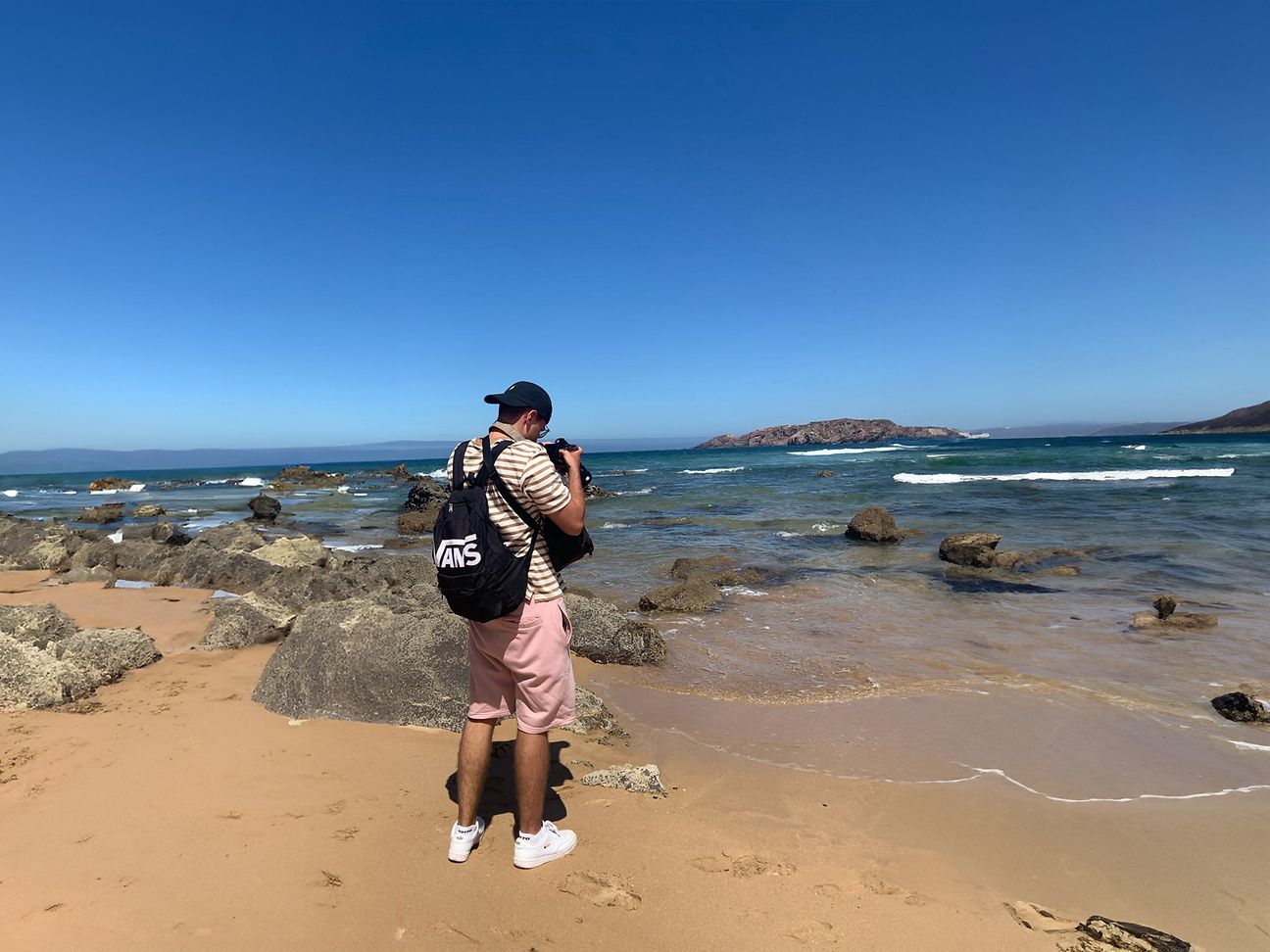 Ein Mann steht am Strand vor dem Meer und fotografiert