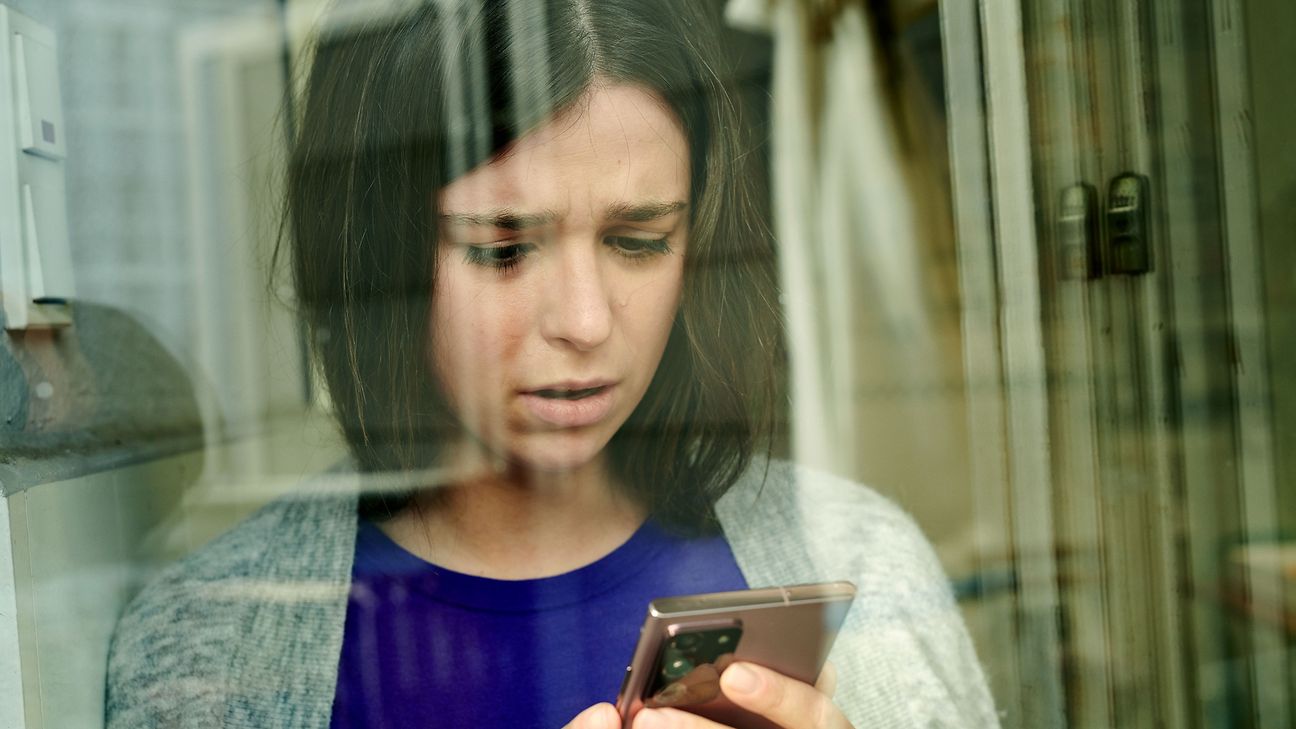 Nachdenkliche junge Frau schaut auf ihr Handy.