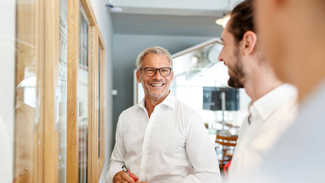 Drei Personen in Businesskleidung unterhalten sich in einem hellen, modernen Büro