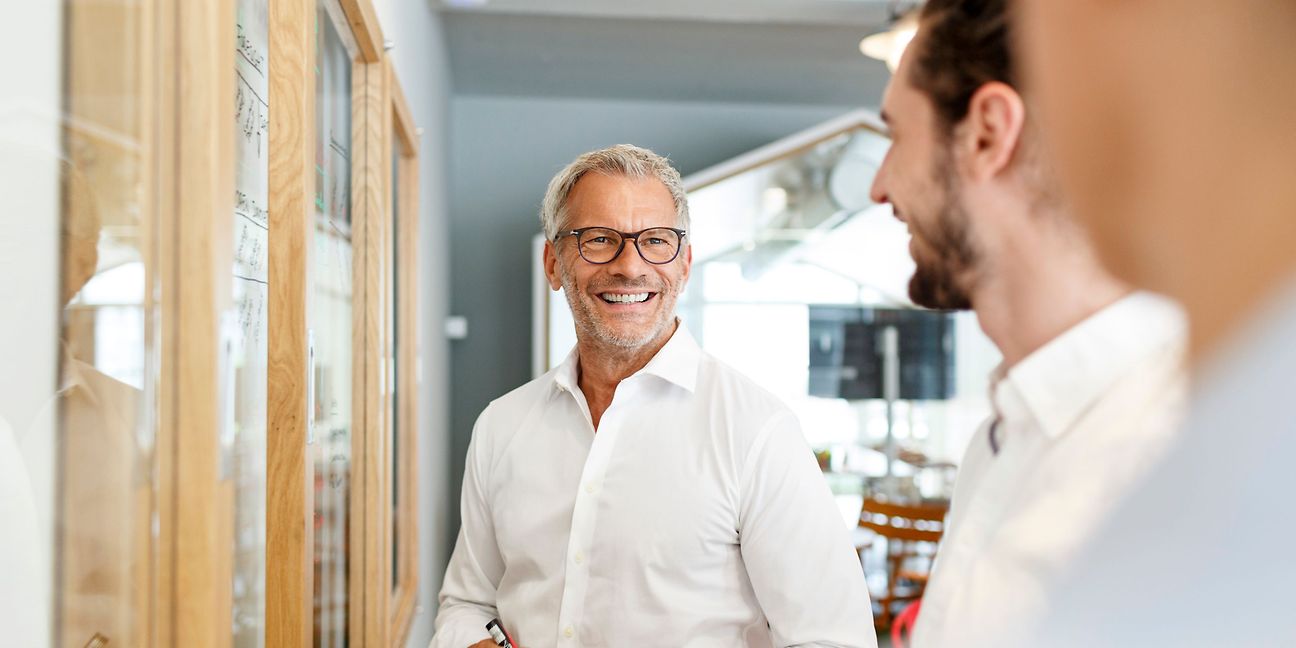 Drei Personen in Businesskleidung unterhalten sich in einem hellen, modernen Büro