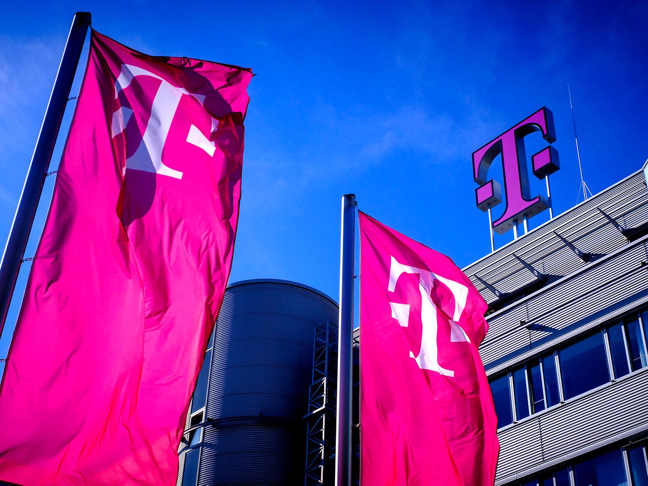 Blick auf ein Telekom Gebäude mit großem Telekom Logo und magentafarbenen Fahnen vor blauem Himmel