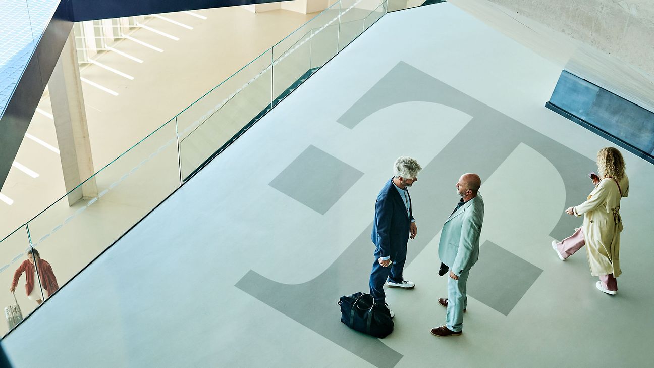 View from above of a wide corridor with a large Deutsche Telekom logo: Two people are talking