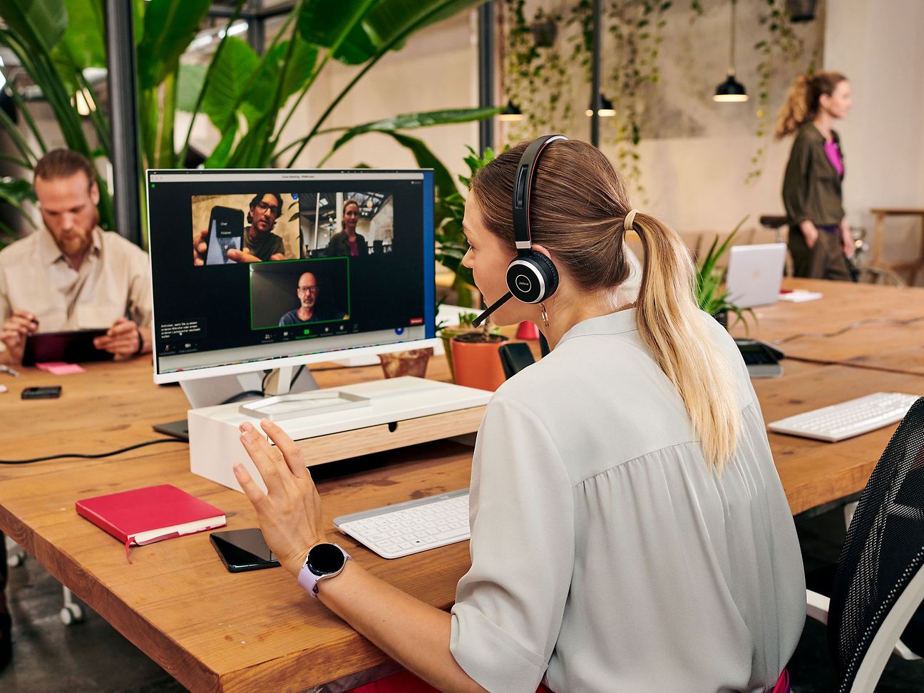 A woman wearing a headset is taking part in an online meeting, three further participants can be seen on her screen