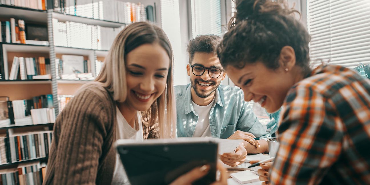 Junge Menschen sitzen fröhlich zusammen und arbeiten gemeinsam am Tablet.
