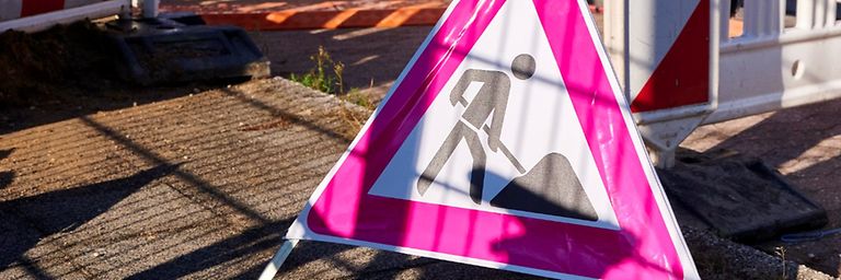 Baustellenschild mit weißen Absperrzäunen, mit weiß-roten Streifen, gelben Warnlichtern