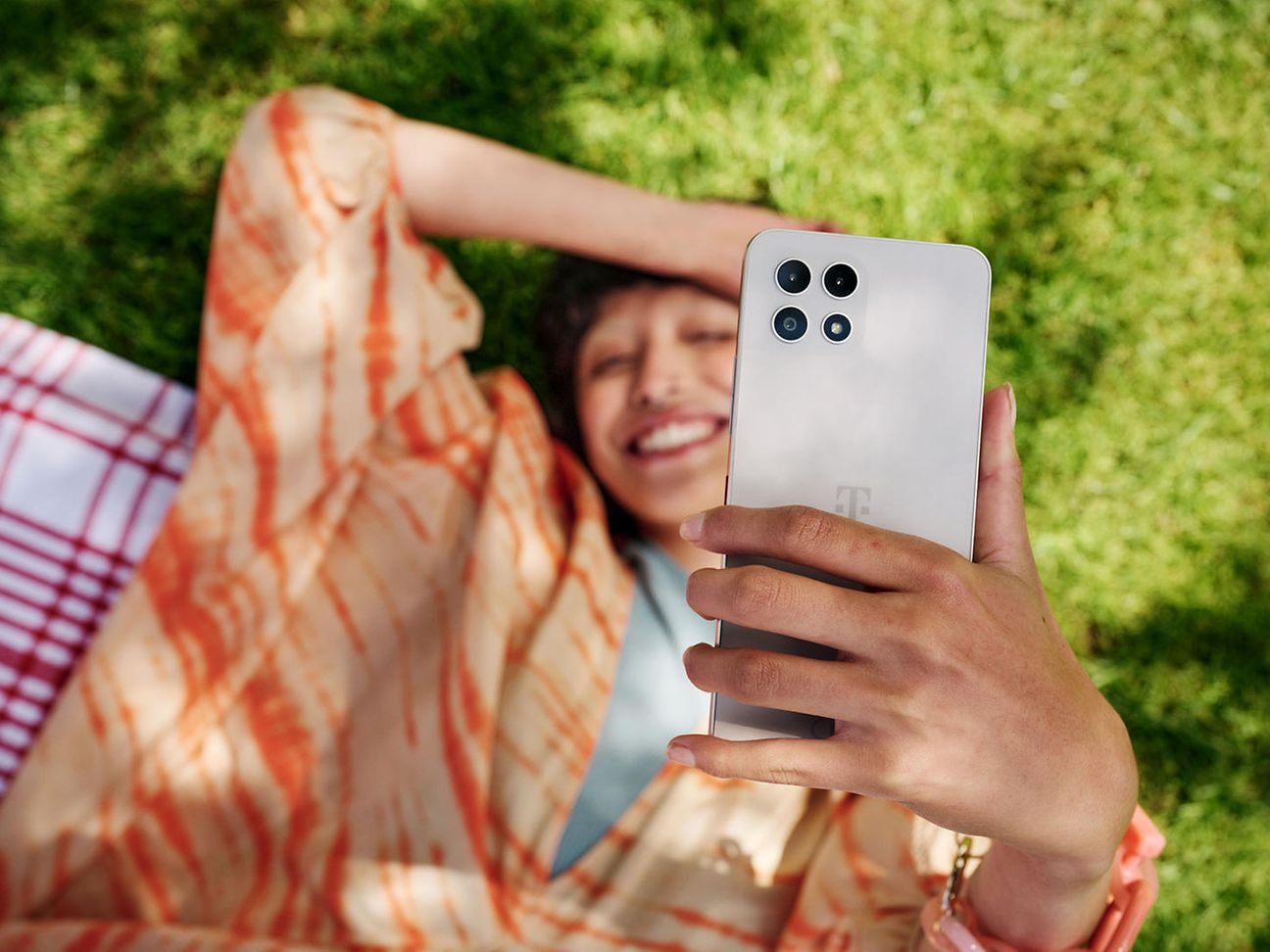 Frau liegt auf der Wiese und lacht und hält ein Handy in die Höhe.