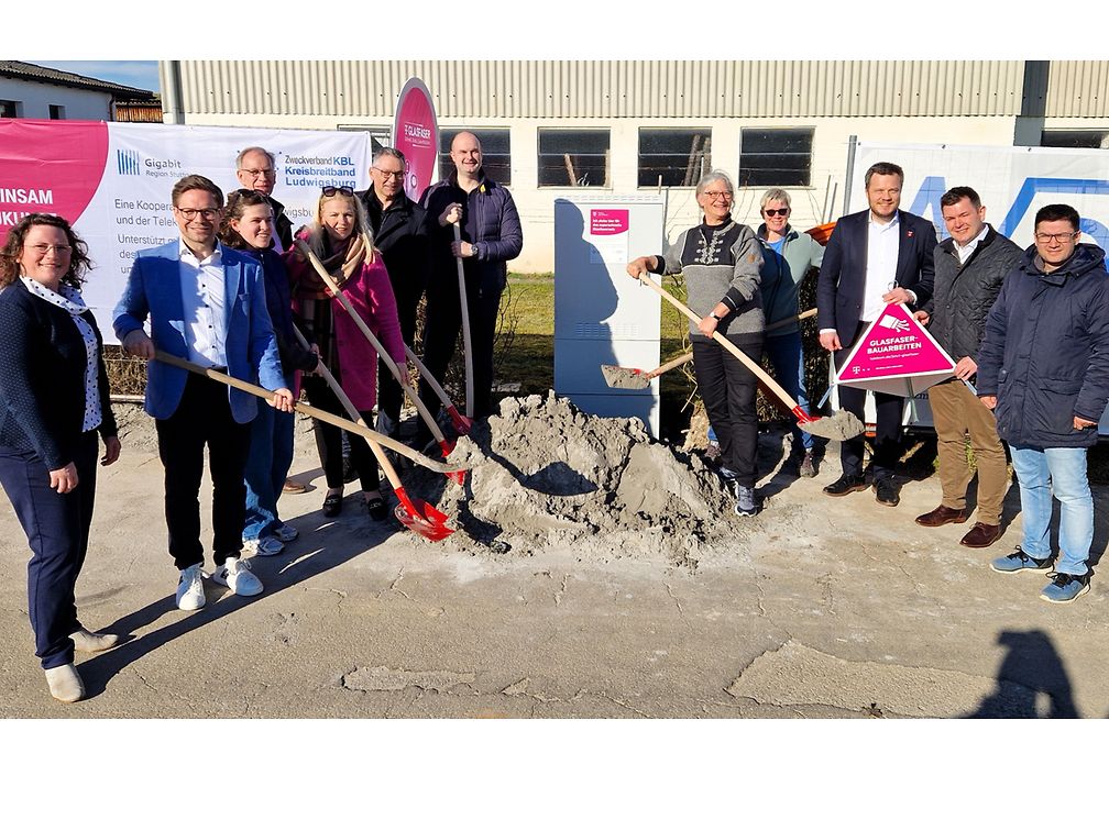 Gruppenfoto vor dem Bauernhof am neuen Netzverteiler, einige schaufeln Sand vom symbolischen Sandhaufen.