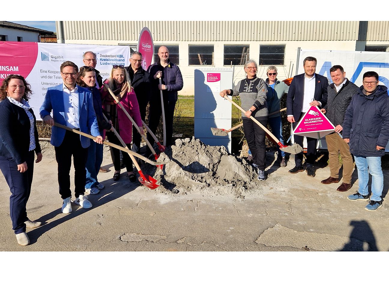 Gruppenfoto vor dem Bauernhof am neuen Netzverteiler, einige schaufeln Sand vom symbolischen Sandhaufen.