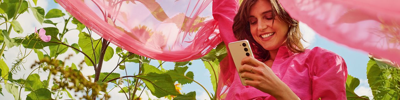 Frau mit Handy und rosafarbenem Schleier steht in einem Blumenfeld.