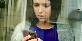 Nachdenkliche Frau schaut auf ein Smartphone.