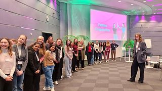 Junge MINT Studentinnen stehen vor einem Präsentations-Bildschirm auf dem „Femtec Cooperation“ steht