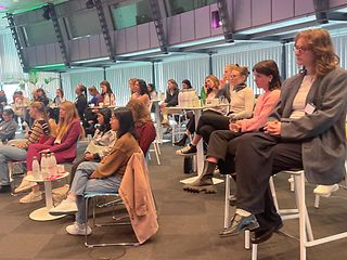 Junge Frauen sitzen in Reihen in einem großen Telekom Raum und verfolgen die Vorträge 