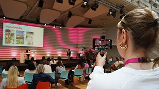 Volunteer films a lecture with her cell phone camera.