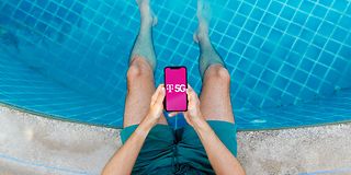 Mann hält Smartphone in Händen und hat die Beine im Pool