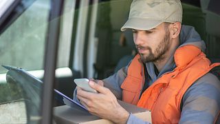 LKW-Fahrer schaut auf Lieferdokument und Handy.