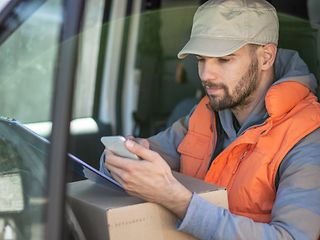 LKW-Fahrer schaut auf Lieferdokument und Handy.