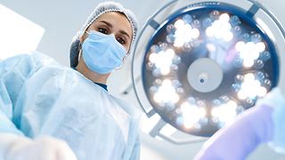 Ärztin beugt sich auf Patienten herunter, großer Beleuchtungsstrahler über ihr.