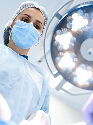 Ärztin beugt sich auf Patienten herunter, großer Beleuchtungsstrahler über ihr.
