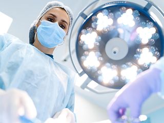 Operating table in operating room, female doctor bending down on patient, large spotlight above her.