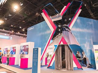 The entrance area at the DIGITAL X trade fair with a large X-shaped pavilion, where people are walking past and entering.