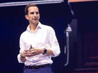 Rodrigo Diehl stands on the main stage in front of a large screen and gives a presentation.