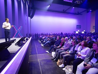 Rodrigo Diehl stands on the main stage in front of a large screen and gives a presentation.