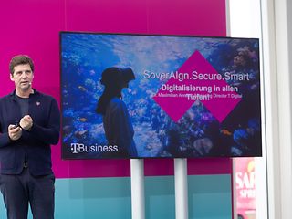Maximilian Ahrens stands on a stage in front of a large screen displaying the title of a presentation on digitalisation. 