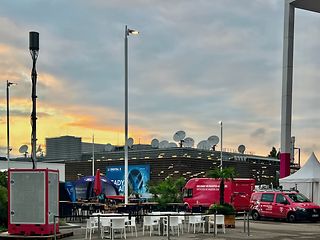 In an outdoor area, a mobile radio mast from Telekom stands next to white seating areas.
