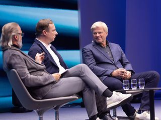 Oliver Kahn, Conrad Dreier and Hannes Händel are sitting on a stage in armchairs and talking as part of a panel discussion. 