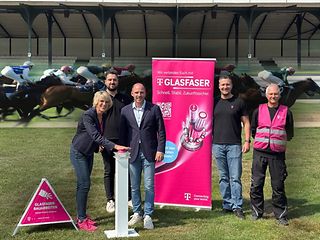 Das Team der Telekom und der Manager der Pferderennbahn stehen gemeinsam auf der Rennbahn.