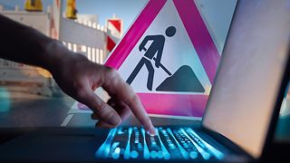 Collage: Eine Hand bedient eine Tastatur eines Computers. Hinten ein "Achtung-Baustelle"-Schild