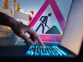 Collage: Eine Hand bedient eine Tastatur eines Computers. Hinten ein "Achtung-Baustelle"-Schild