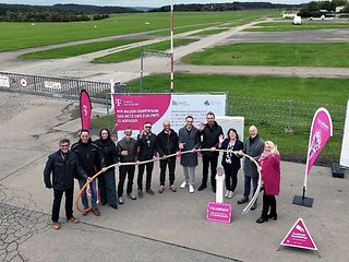 Gruppenaufnahme der Beteiligten aus der Vogelperspektive. Im Hintergrund die Start- und Landebahn des Flughafens Hahnweide. 