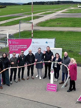 Gruppenaufnahme der Beteiligten aus der Vogelperspektive. Im Hintergrund die Start- und Landebahn des Flughafens Hahnweide. 