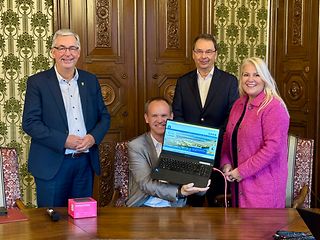 Bürgermeister Schäfer zeigt den Laptop mit magenta LAN-Kabel 