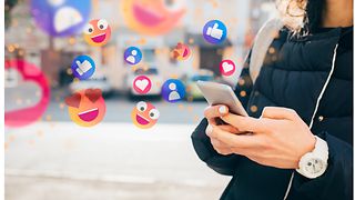 A mobile phone in the hand of a person with various emojis