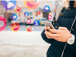 A mobile phone in the hand of a person with various emojis