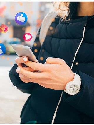 A mobile phone in the hand of a person with various emojis