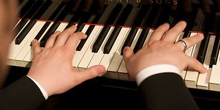 Nahaufnahme von zwei Händen, die auf einem Flügel Klavier spielen.