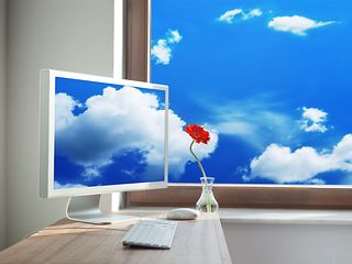 Ein Rechner auf einem Schreibtisch. Die Wolken, die draußen am Fenster vorüber wehen, fließen in den Bildschirm.