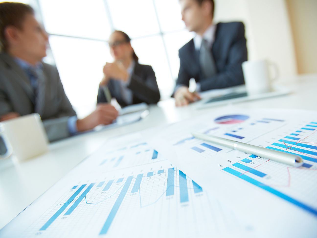 Team im Hintergrund diskutiert über Präsentation von Diagrammen im Vordergrund