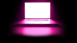 Laptop illuminated magenta before black background.