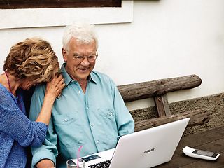 Älteres Paar mit Laptop sitzt auf einer Bank.
