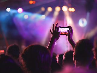 Man in an audience is taking a photograph with his smartphone.