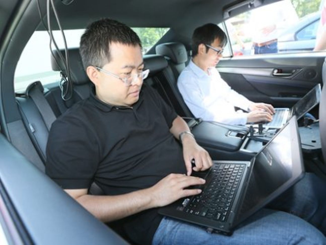 Zwei Männer mit Laptop auf Rücksitz eines Autos