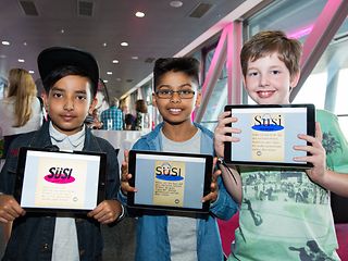 Three boys holding up tablets