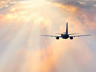 Flugzeug fliegt in von Wolken verhangenen Sonnenaufgang