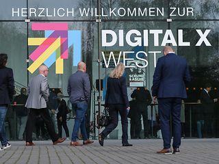 Digital X West Logo mit Teilnehmern, die den Veranstaltungsort betreten.