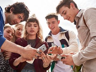 Junge Menschen stehen im Kreis halten die Smartphones in die Mitte, diskutieren über die Inhalte